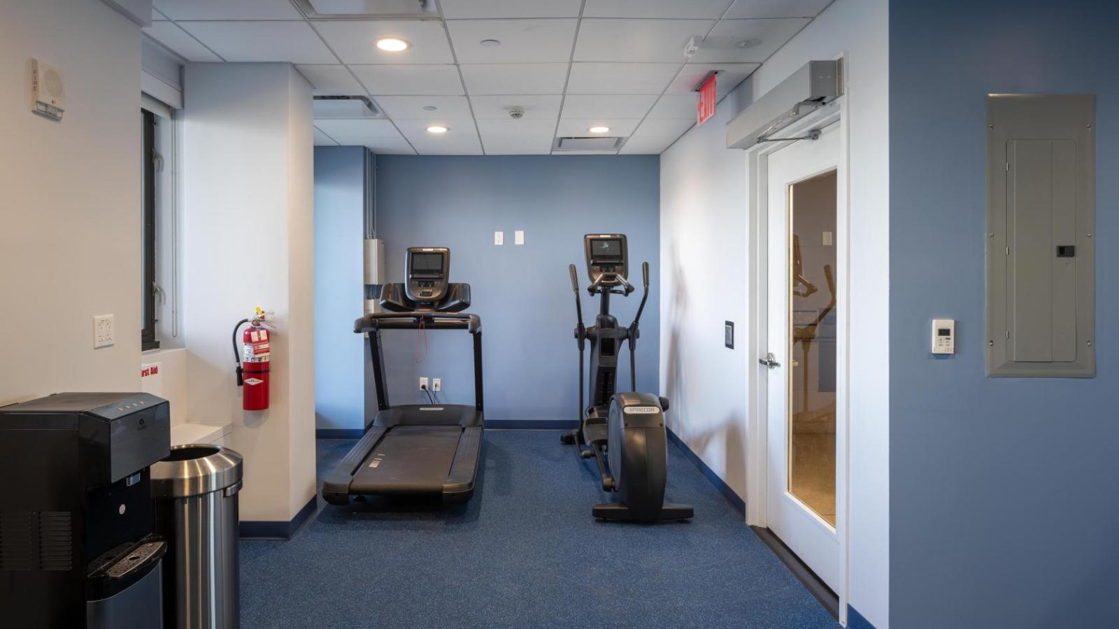 A treadmill machine and an elliptical machine are located next to each other on a blue floor