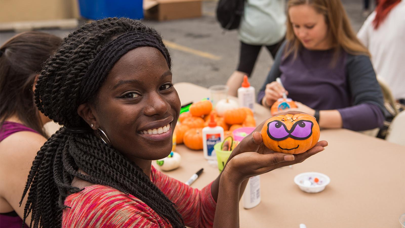 A young woman holding up a decorated pumpkin
