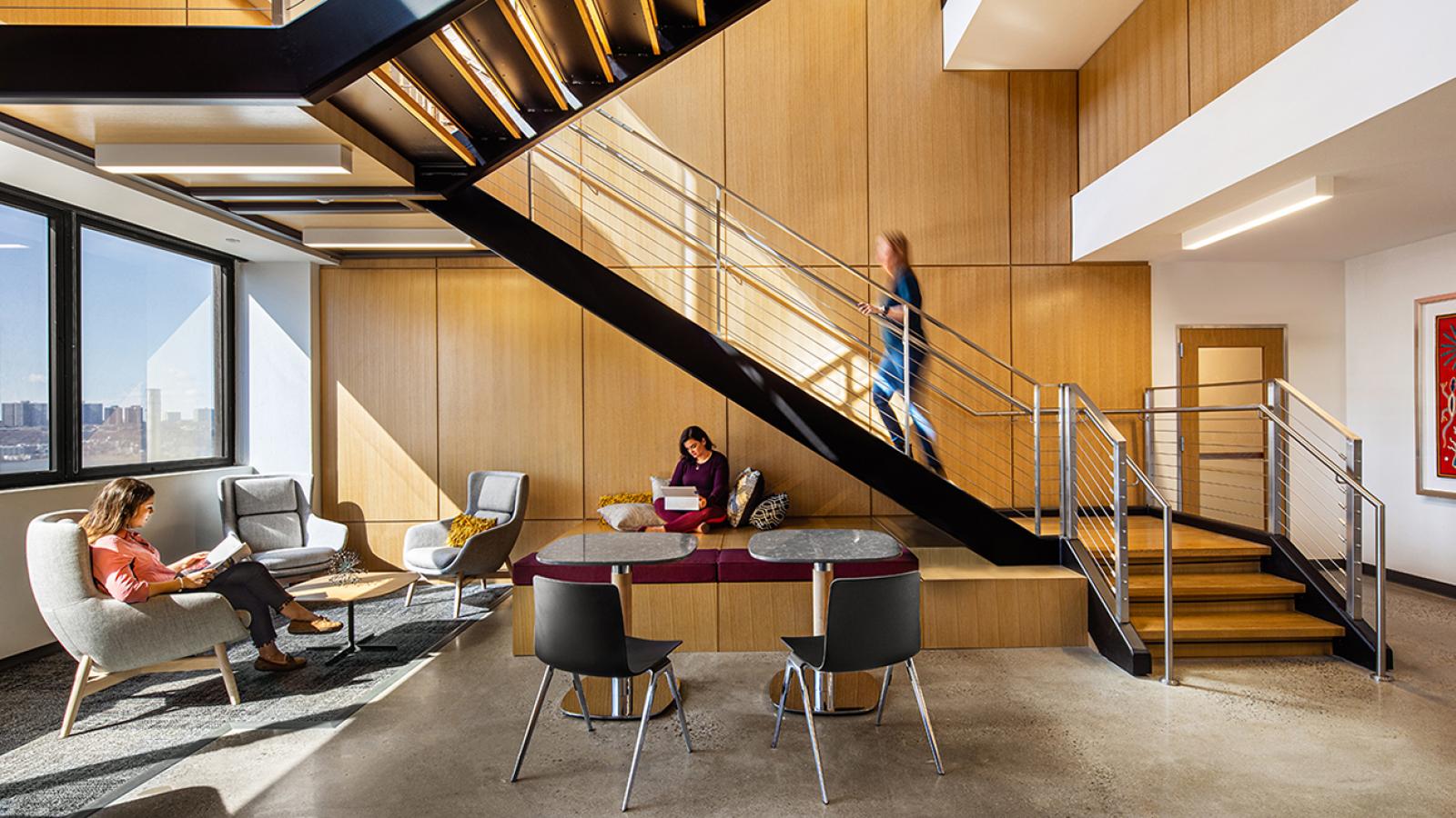 Two people sit in individual chairs while one other person walks up a staircase