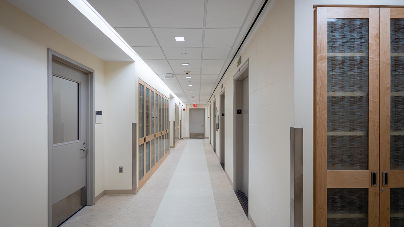 An empty hallway with view of doors, elevator, and storage closets