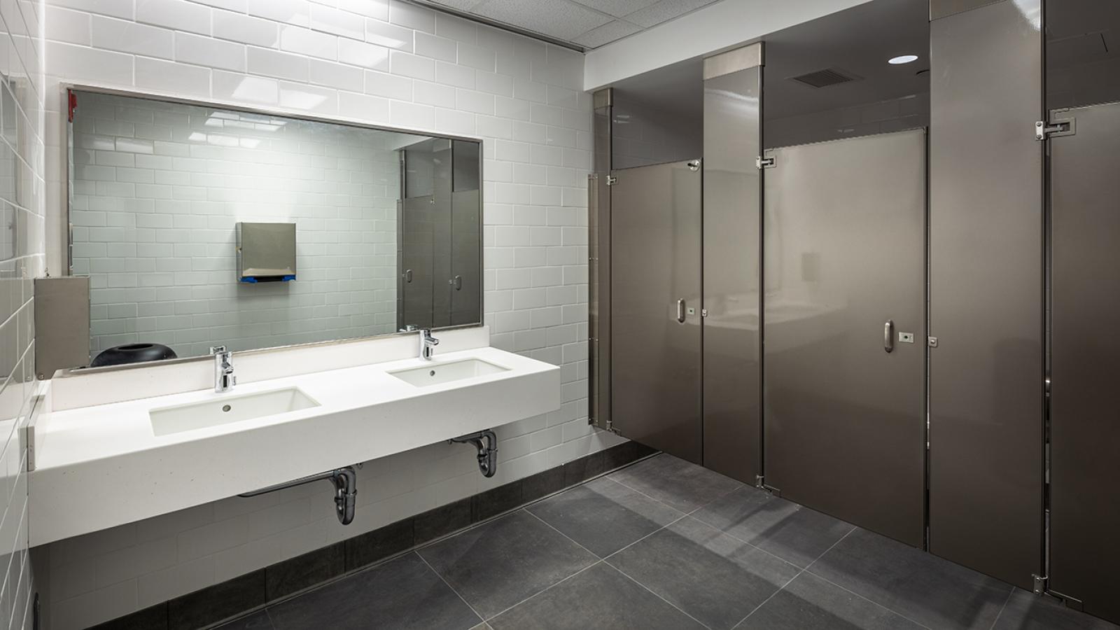 A women's bathroom with mirror, two sinks, and three stalls.