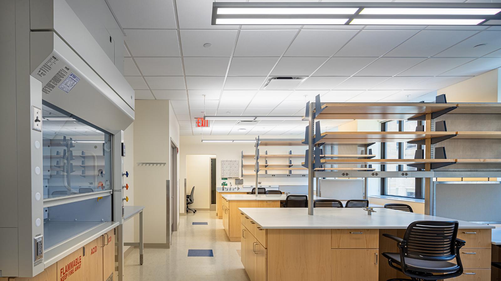 A picture of a lab with desks, a fume hood, and shelves