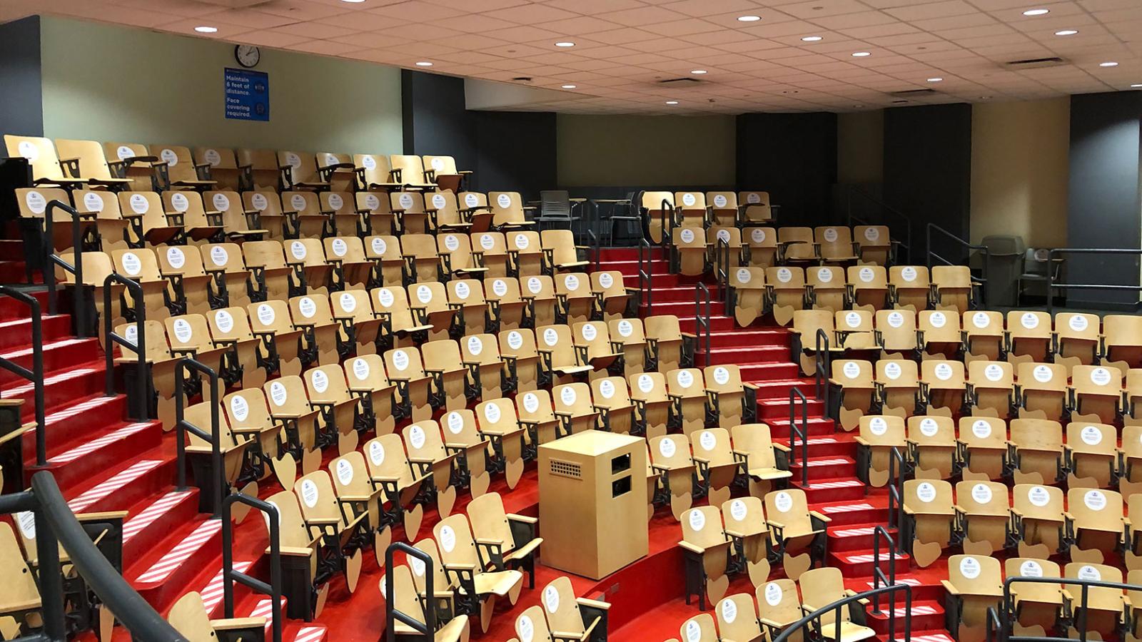 An amphitheater filled with rows of wooden chairs with stickers on the chair backs