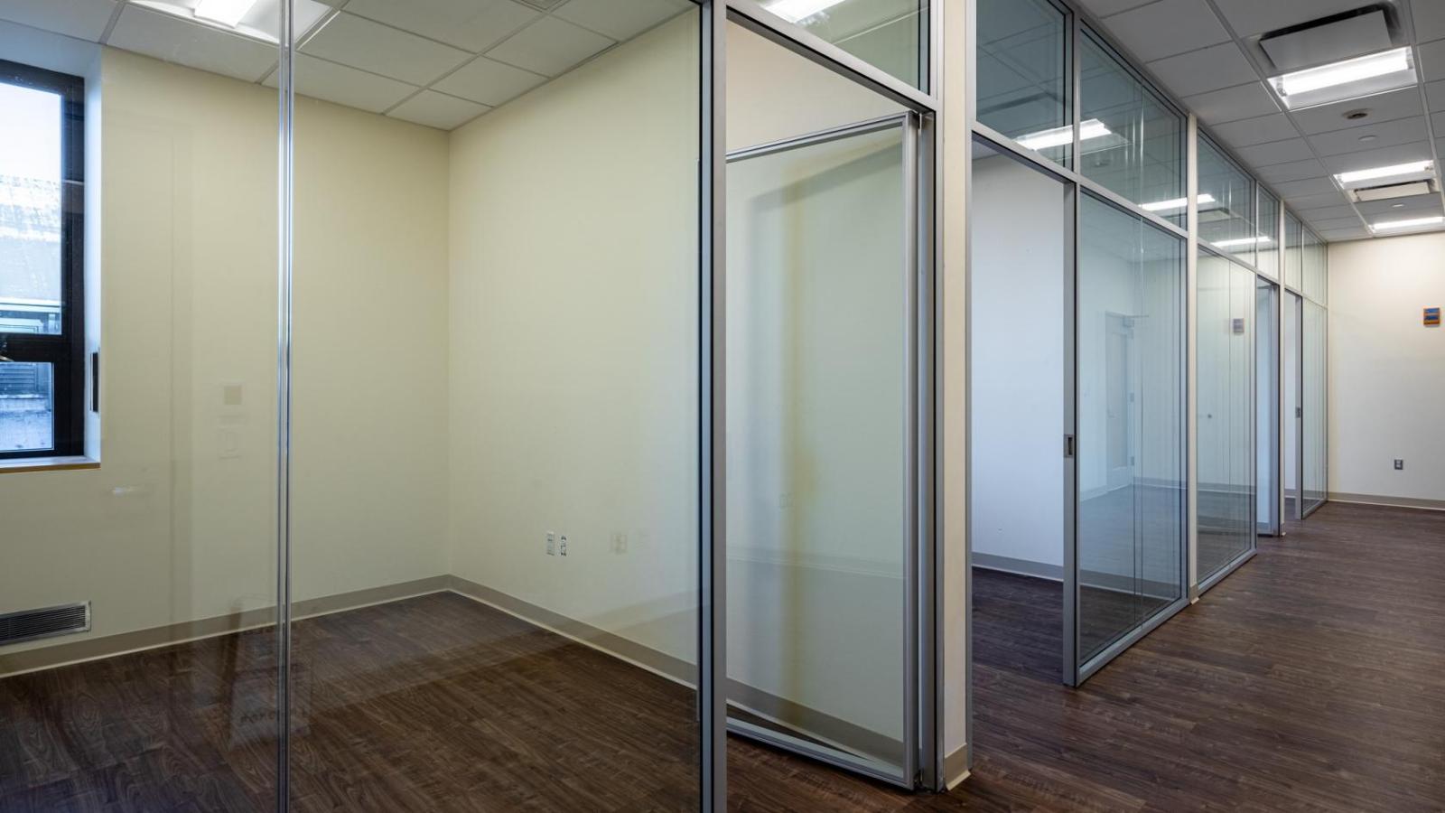 Several rooms with glass walls align a dark wood floor hallway