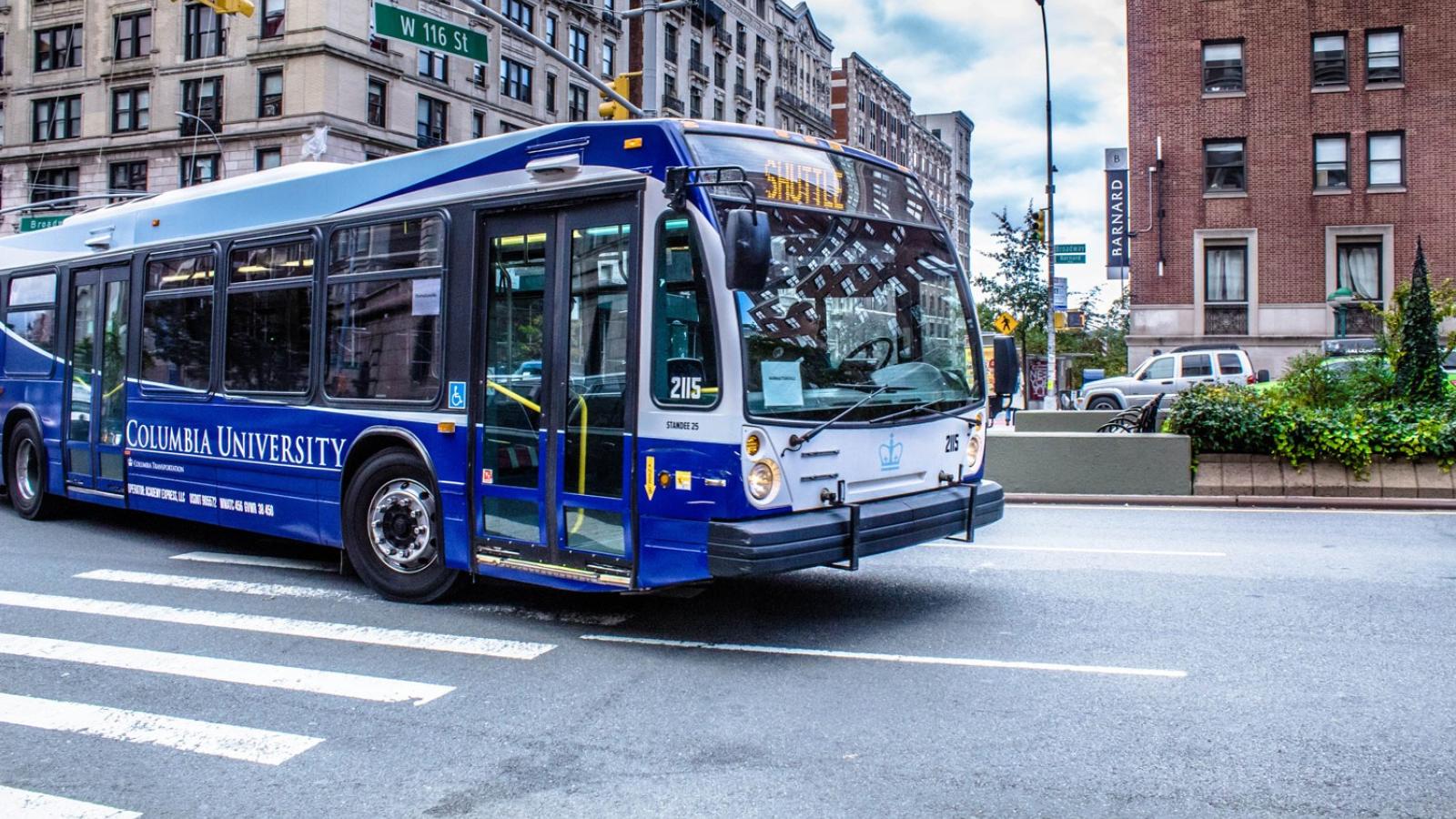 A blue Columbia University intercampus shuttle bus drives at the intersection of 116th Street and Broadway