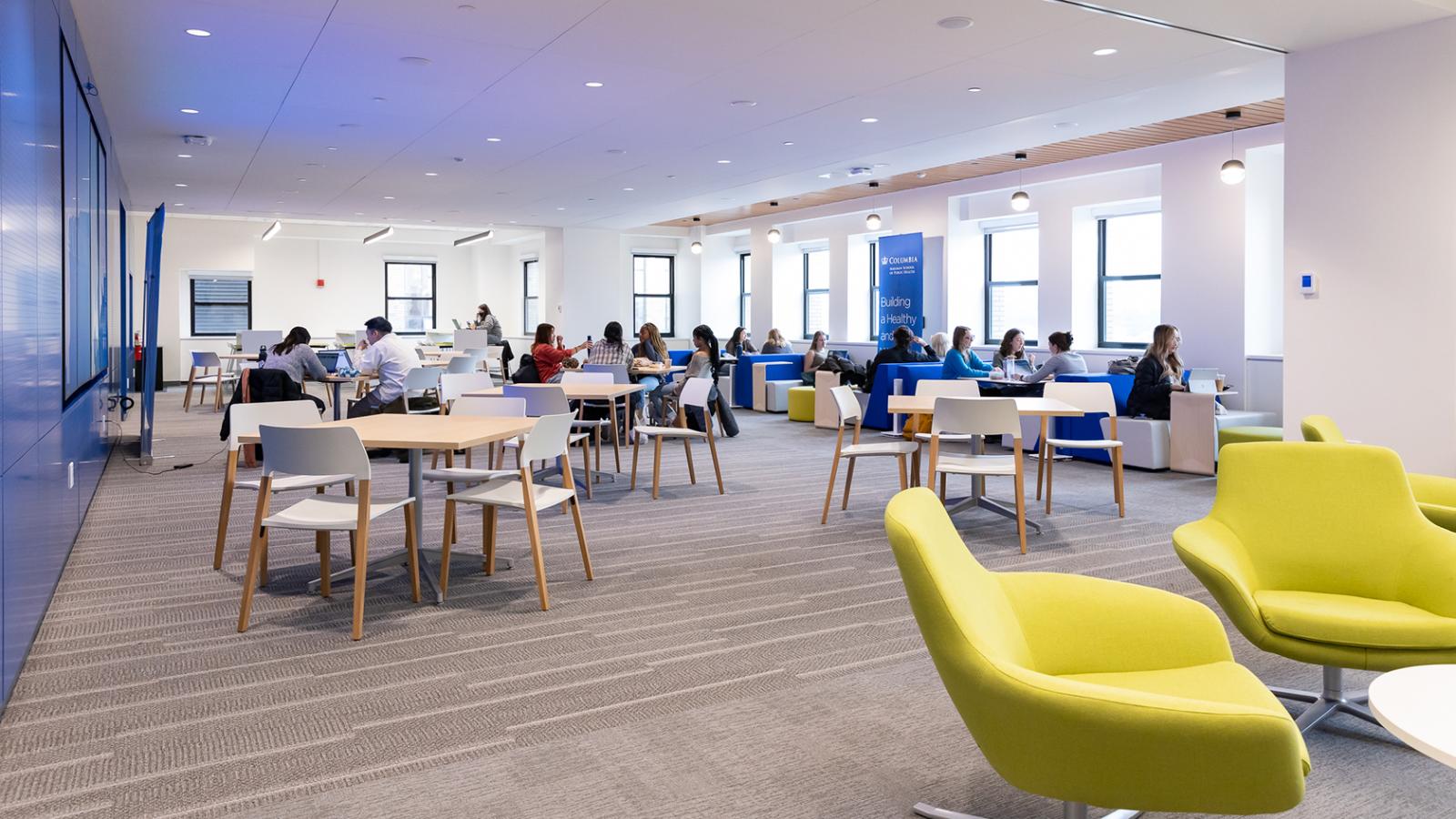 A room with two citrine chairs in the lower right corner and wooden circle table with people sitting around them.