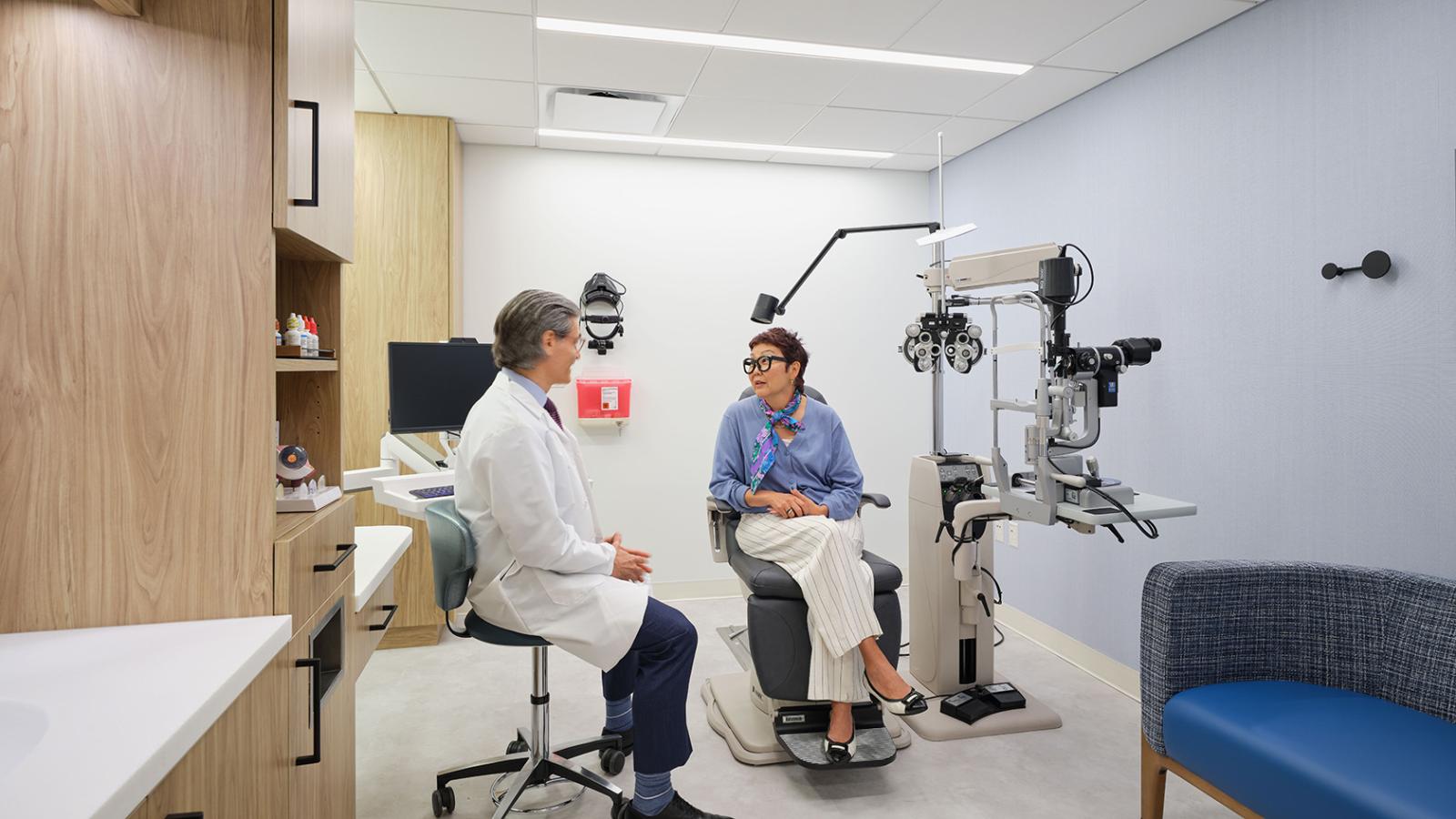 Physician and patient in a modern ophthalmology exam room with wood cabinetry, medical equipment, and calming finishes.