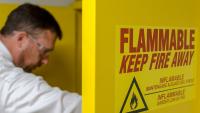 A member of Campus Life Safety and Regulatory Compliance wearing safety goggles while checking a cabinet with flammable liquids
