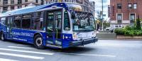 A blue Columbia University intercampus shuttle bus drives at the intersection of 116th Street and Broadway
