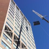 A tower crane lifting a new air conditioner onto the room for the Hammer Health and Sciences building.