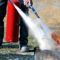 An individual uses a fire extinguisher to put out a fire outdoors.