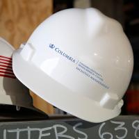 Two safety helmets on a shelf, one with the american flag, the other with the Facilities Management logo.
