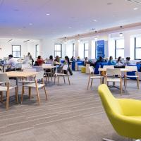 A room with two citrine chairs in the lower right corner and wooden circle table with people sitting around them.