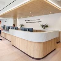 Reception desk at the Robert Burch Family Eye Center with wood and marble finishes, staff assisting a patient, and a seating area in the background.