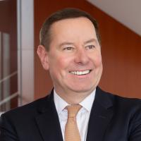 Patrick Burke looks away and smiles while wearing a dark suit and light colored tie