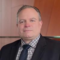 Eric Lorenzen wearing a dark jacket and tie with a grey checkered button-down shirt